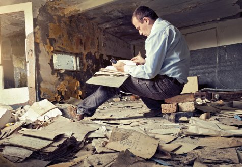 Man sitting in dilapidated room surrounded by taxes papers. 