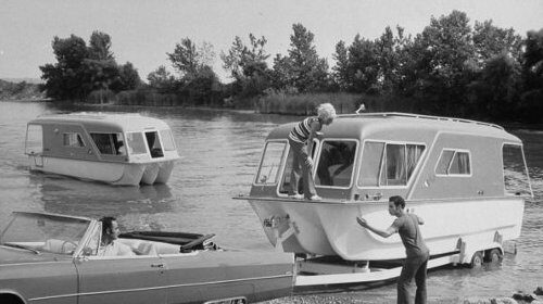 An old photo of a man towing a camper trailer.