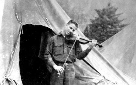 A disciplined man playing a violin in front of a tent.