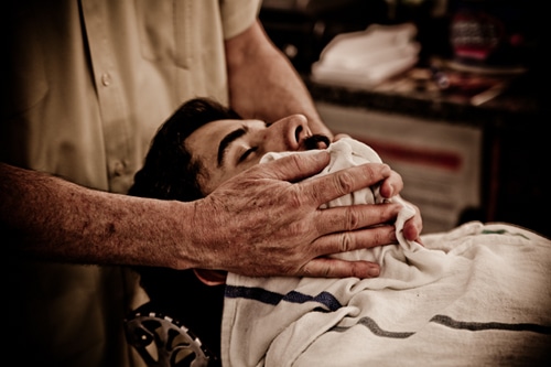 Barber cleaning the man's face with warm towel.