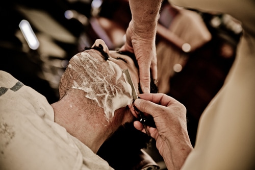 Barber removing shaving cream using razor blade.