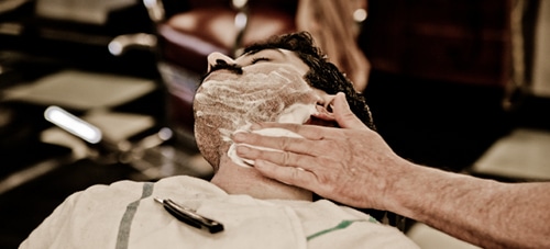 Barber applying shaving cream on man's face.
