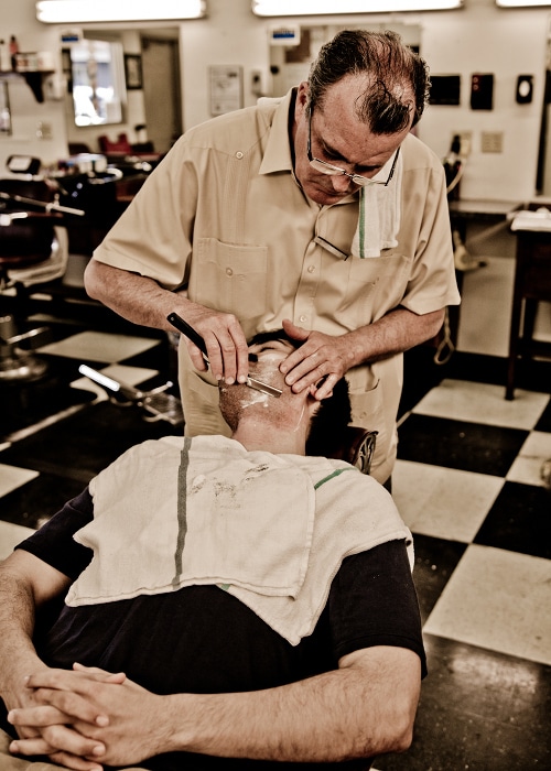 Barber cleaning the face of man by using razor blade.