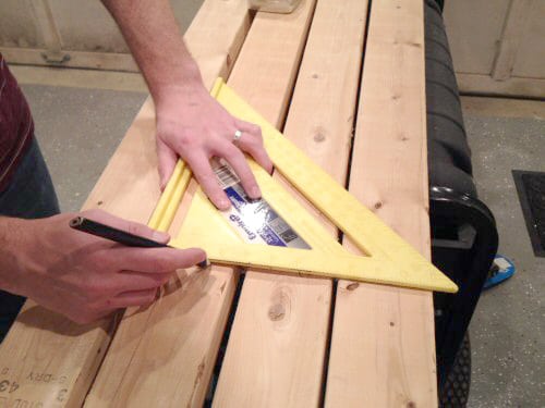 Man taking measurements of table using scale and pencil.