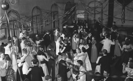 This black and white photo captures a group of young men and women elegantly dancing in a ballroom.