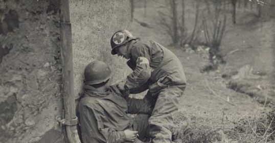 An old photo of a Combat Medic helping another soldier.