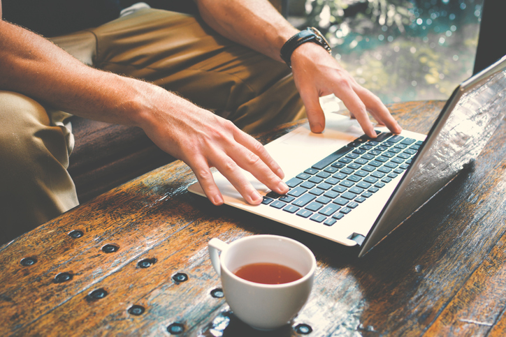 A man writing on a laptop with a cup of tea.