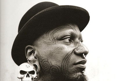 A **tattoo artist** with a skull **tattoo**, captured in a black and white photo.