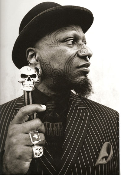 A **tattoo artist** with a skull **tattoo**, captured in a black and white photo.