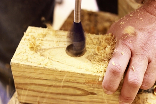 Man boring the holes in wooden piece.