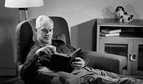 A man engrossed in a fiction book, reading while comfortably seated in a chair.