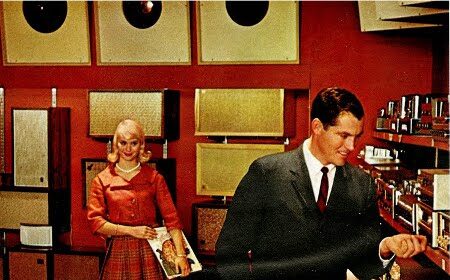 An American bachelor and his companion standing next to a record player from the 20th and 21st century.