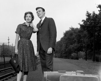 A black and white photo of a man and woman with travel luggage.
