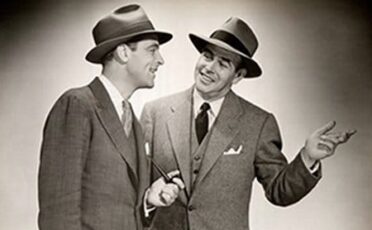 Two men in suits and hats engage in a conversation to improve their techniques.
