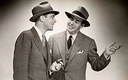Two men in suits and hats engage in a conversation to improve their techniques.