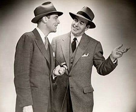 Two men in suits and hats engage in a conversation to improve their techniques.