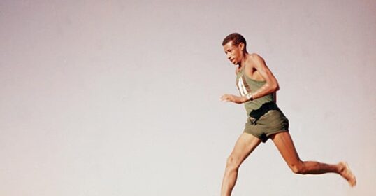 An old photo of a man running barefoot in the desert, accompanied by FAQ's.