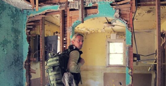 A man with a backpack standing in a demolished room, carrying his Get Home Bag