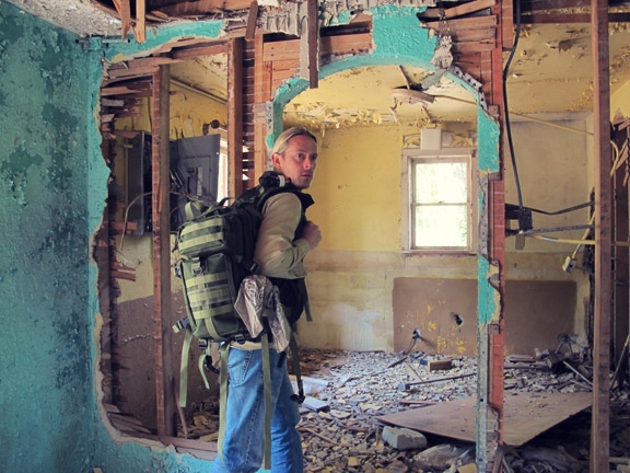 A man with a backpack standing in a demolished room, carrying his Get Home Bag