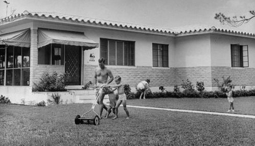 A black and white photo of children playing in the yard of a house.