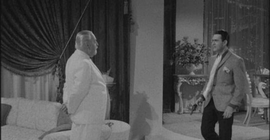 Two men standing next to each other in a sweet living room.