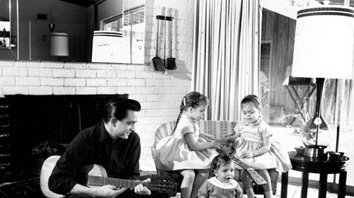 A black and white photo of a dad and his children in a living room, singing songs together.