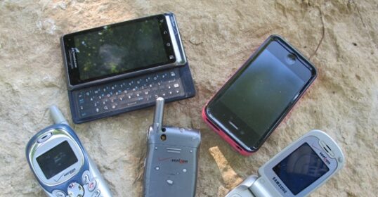 A group of BUSTED cell phones laying on a rock.