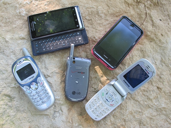 A group of BUSTED cell phones laying on a rock.