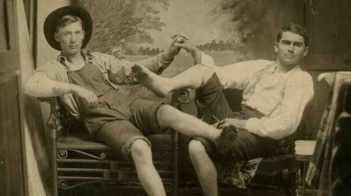 An old photo showing two men sitting on a chair, displaying their male affection.