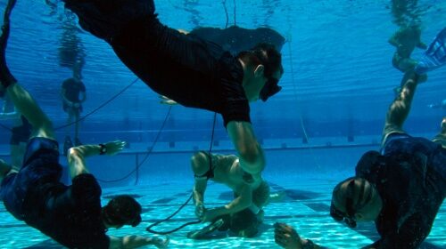 A group of Navy SEALs practicing their underwater knot tying skills in a swimming pool.