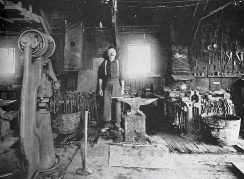 Vintage man blacksmith in shop behind anvil.