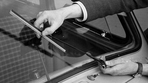A man troubleshooting common problems with his car window, using a pair of scissors to open it.