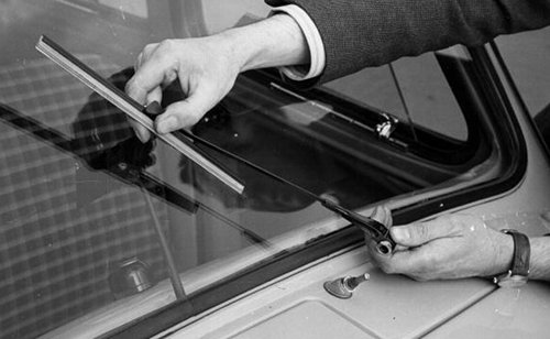 A man troubleshooting common problems with his car window, using a pair of scissors to open it.