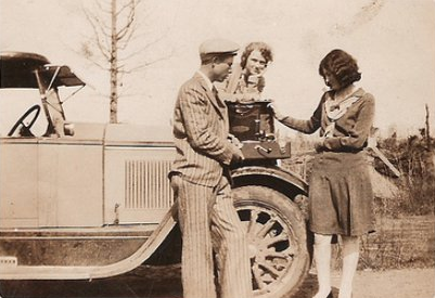 An old photo of a man and woman standing next to a car.