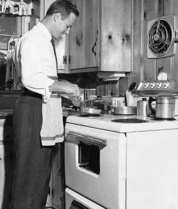 Vintage man cooking on stove smiling.