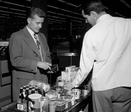 Vintage man at grocery store counter paying for food.