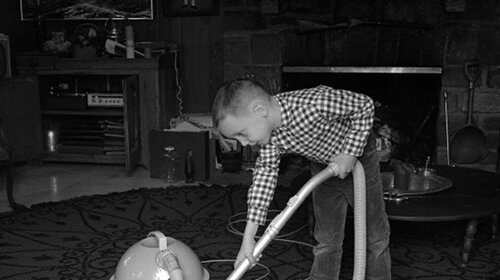A young boy mastering the art of dadliness by using a vacuum cleaner for chores in the living room.