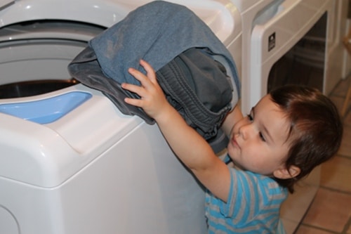 Young boy putting clothes laundry in washer doing chores. 