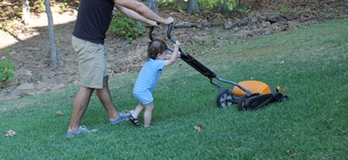Young boy helping dad mow lawn. 