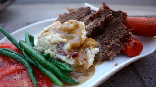 A delicious Sunday supper featuring pot roast with meat, potatoes, and green beans, served alongside creamy mashed potatoes.
