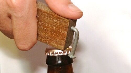 A handy person using a wooden bottle opener to open a beer bottle.