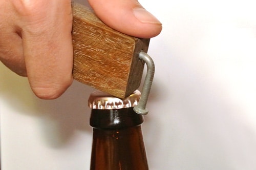 A handy person using a wooden bottle opener to open a beer bottle.