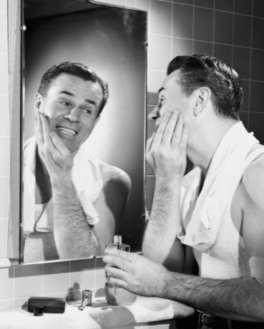 Vintage man looking in mirror after shave smiling. 