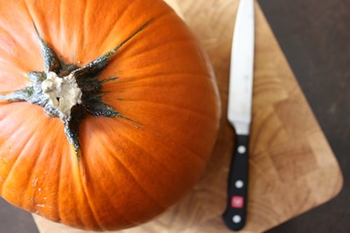 Whole pumpkin on cutting board next to knife .
