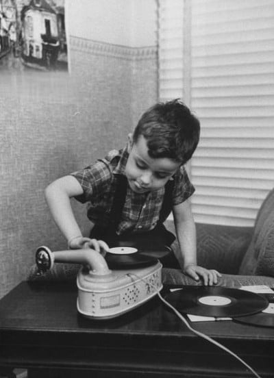 Vintage kid boy putting record onto turntable. 