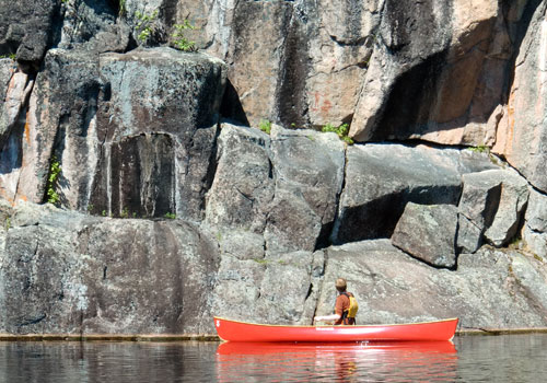 Red canoe on lake in front of cliff face bwca.
