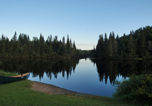 Canoe on shore of small lake trees blue sky.