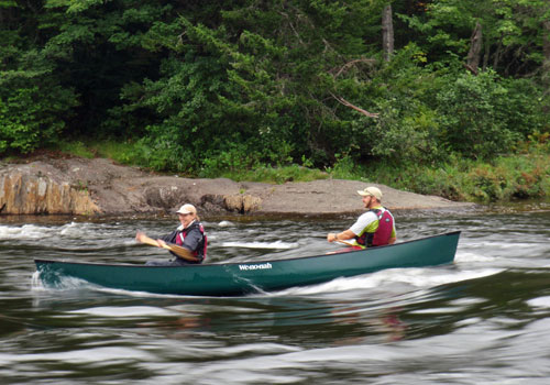 Two people canoeing on swift river.