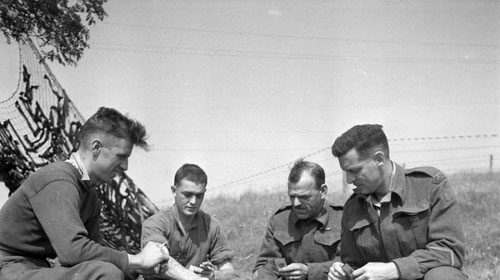 A group of manly men sitting on a blanket playing cribbage.