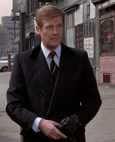 James Bond Roger Moore outdoors wearing black overcoat.